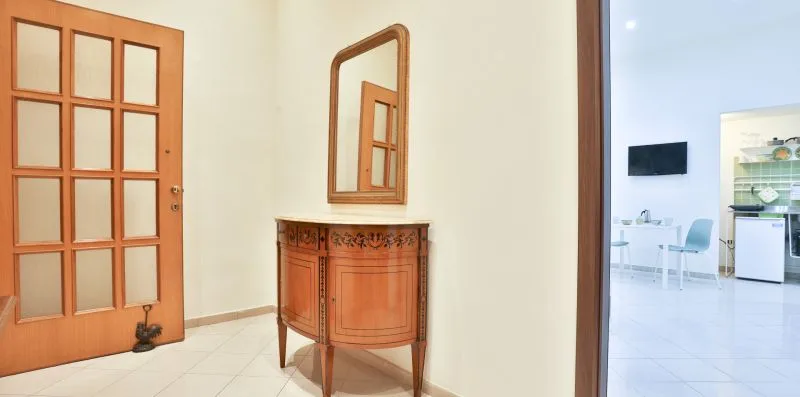 A wooden cabinet and mirror stand beside a doorway to a bright room.