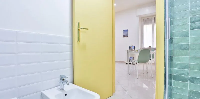 A bathroom doorway opens onto a bright room with a desk and chair.