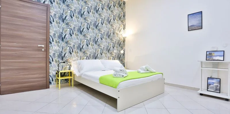 A bedroom with a white bed, bright green bedding, and patterned wallpaper.