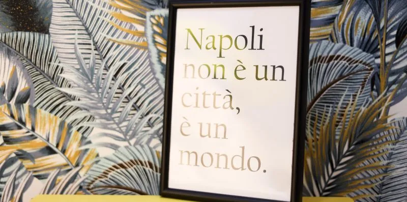 A framed Italian quote hangs against patterned botanical wallpaper.