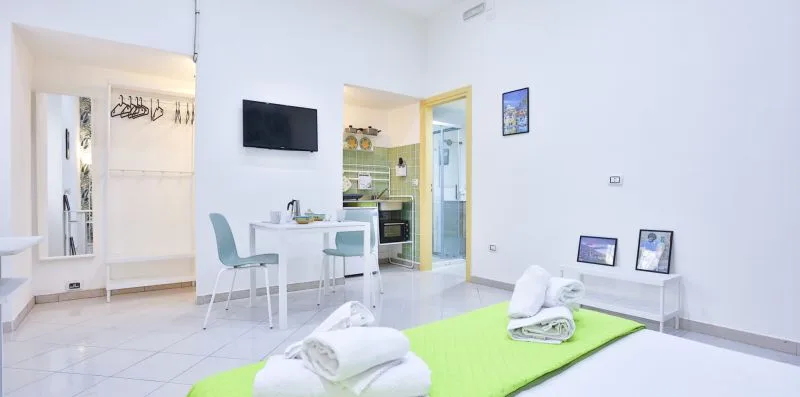 A bright room with a dining table, wall-mounted television, and folded towels on a green mat.