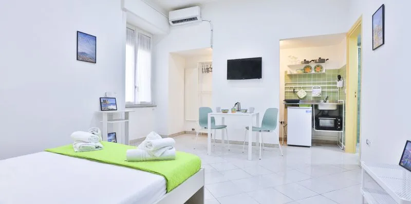 A bright bedroom with a green bed, a small dining table, and a kitchenette.