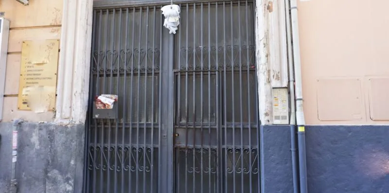 A building entrance with a tall metal gate and notice boards on the walls.