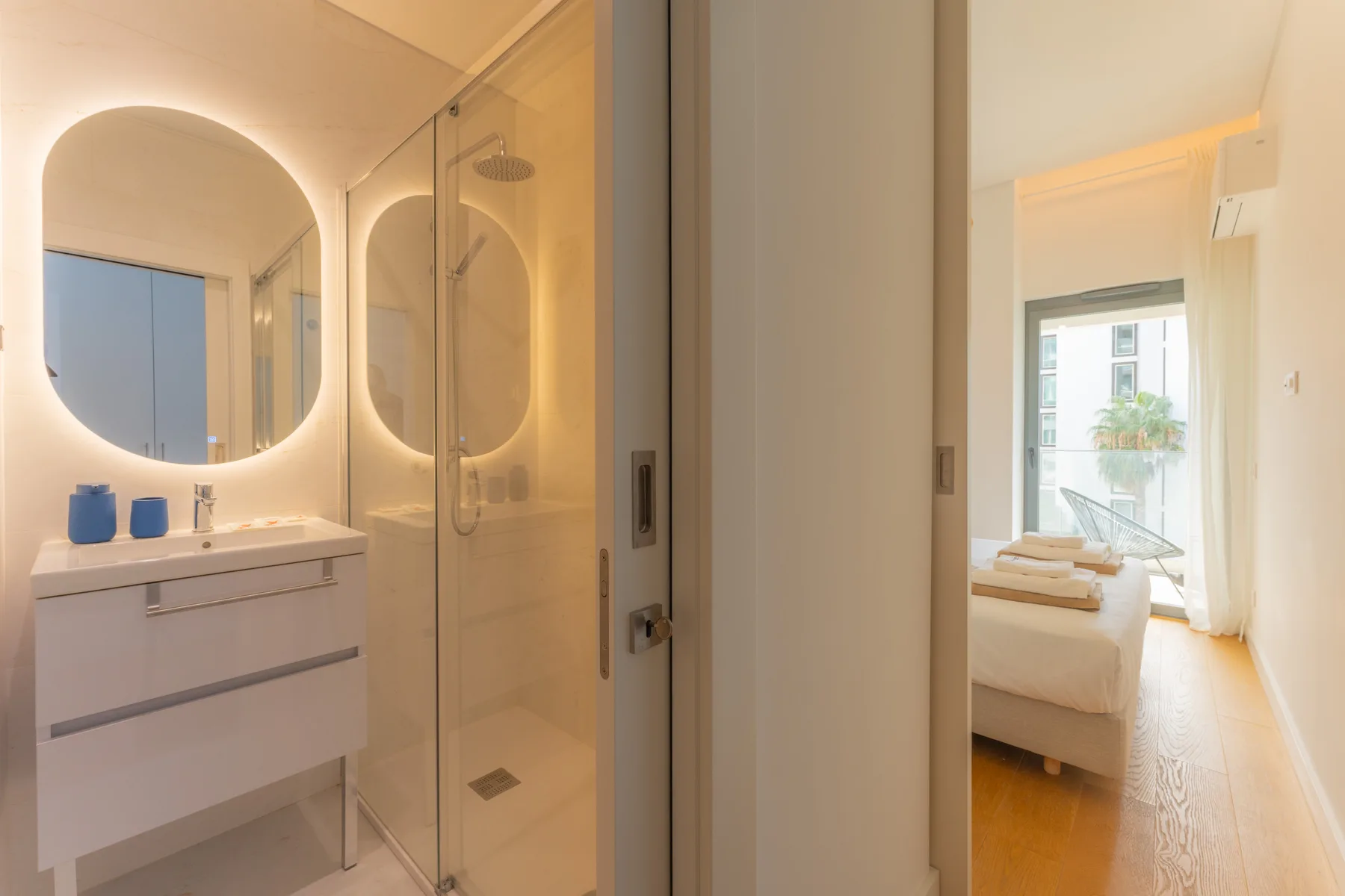 Un baño con ducha de vidrio y vista a un dormitorio luminoso.
