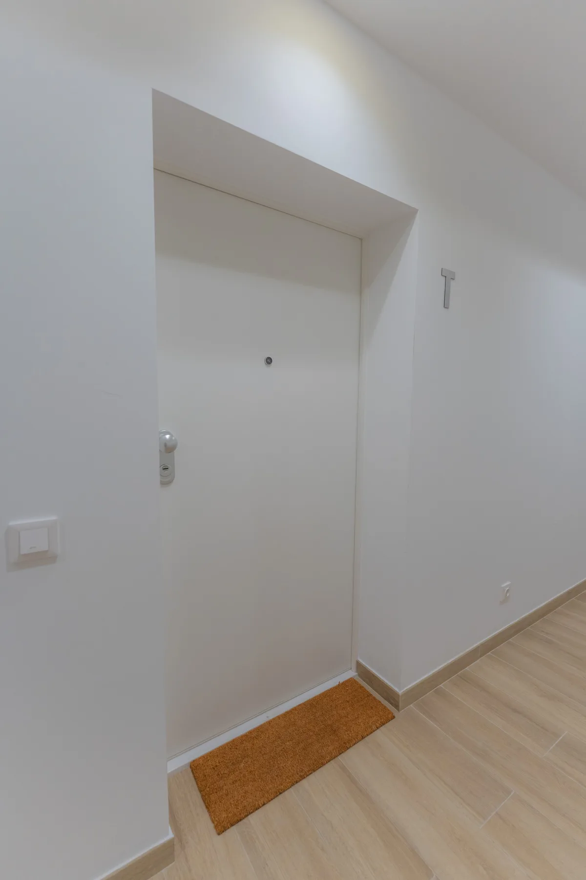Una puerta blanca da a un pasillo con suelo de madera clara.