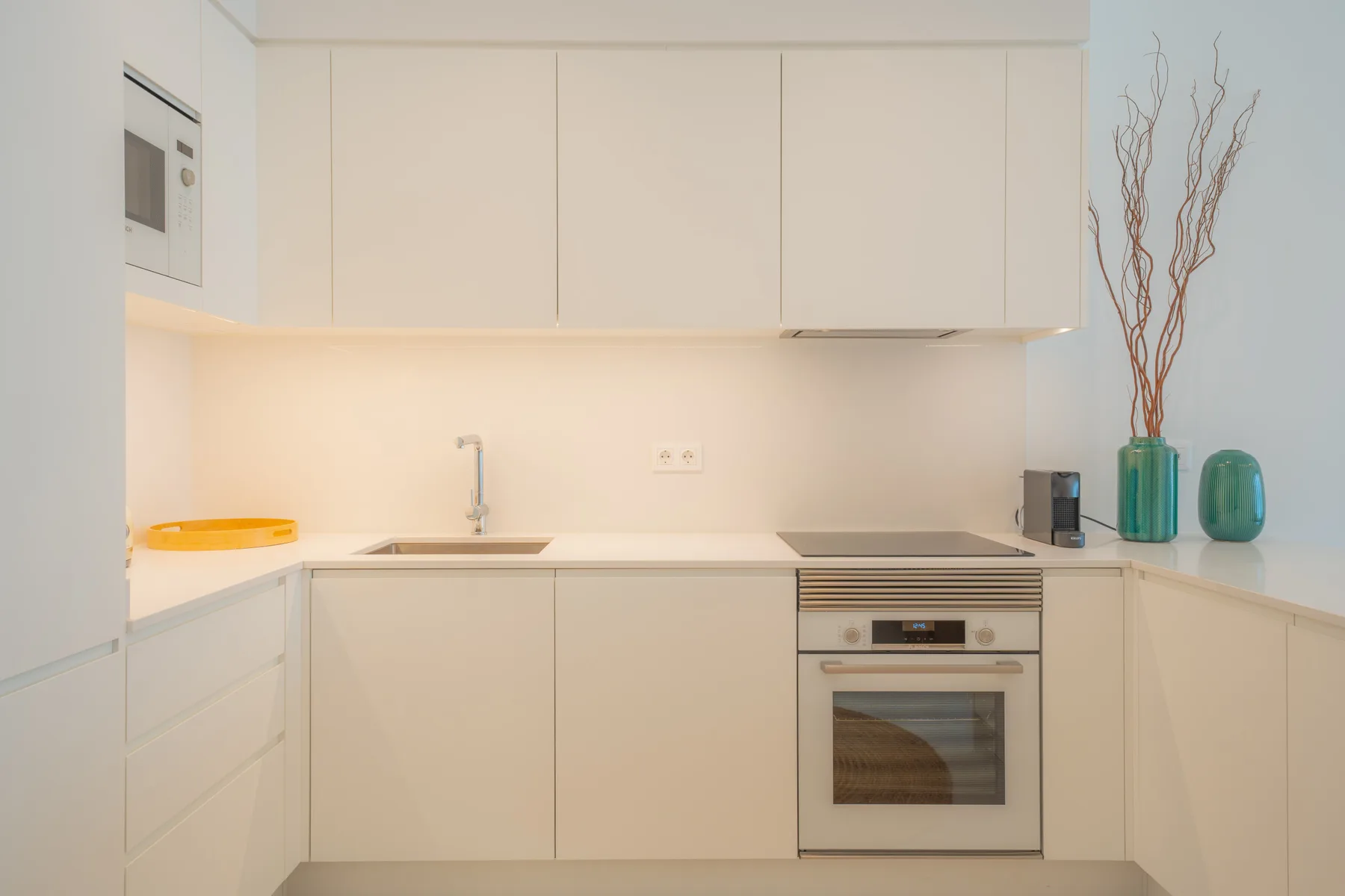 Una cocina moderna y luminosa con armarios blancos y un horno integrado.