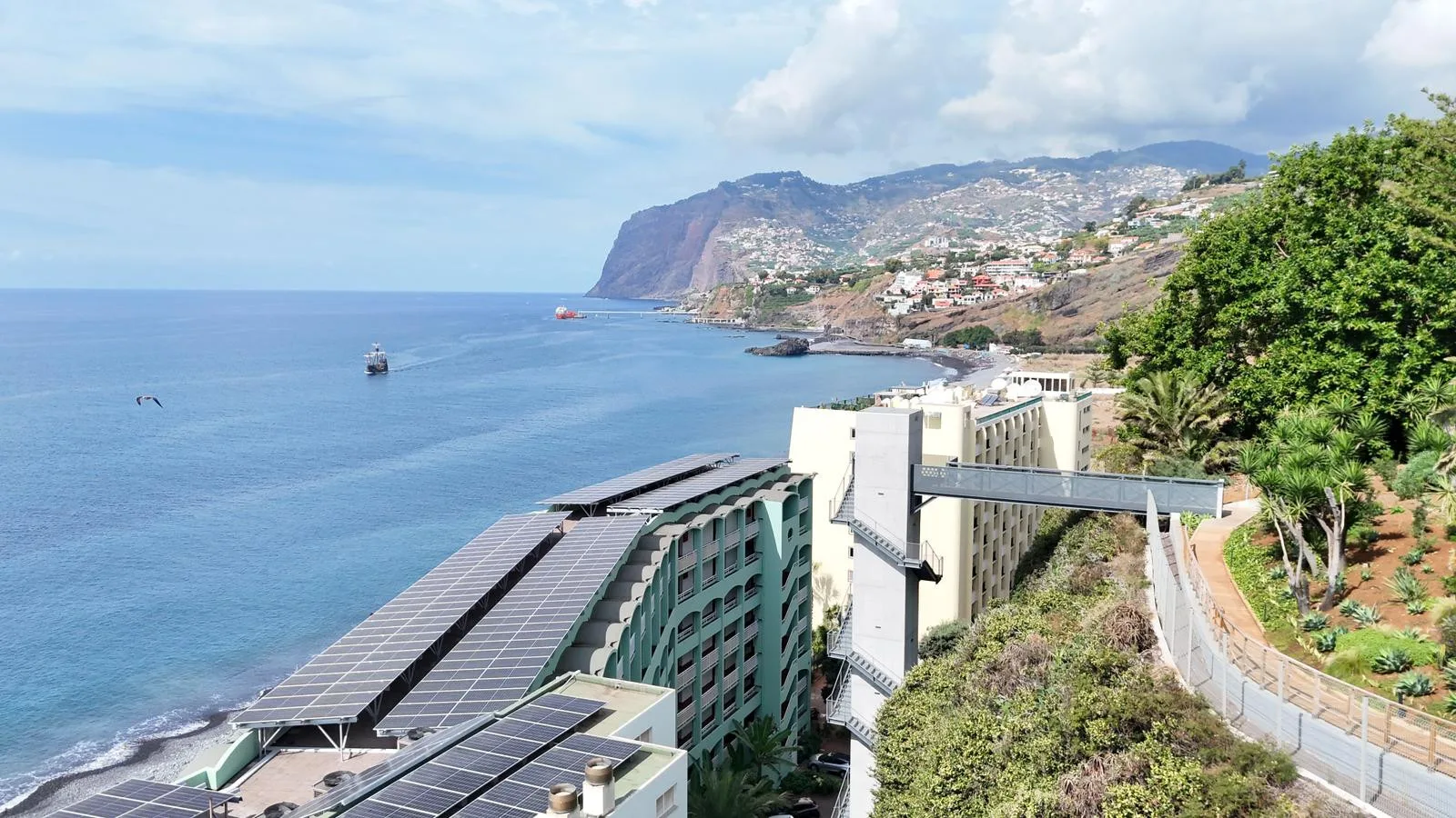 Paisaje costero con vista al océano, edificios en la ladera y un complejo junto al agua.