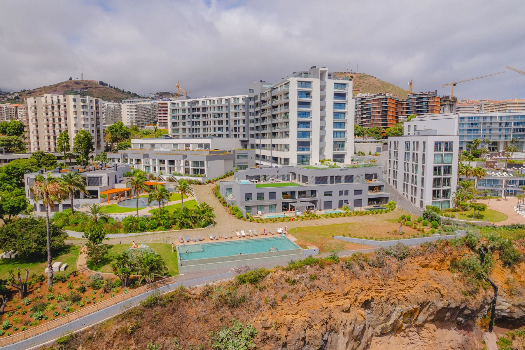 Edificios de apartamentos modernos y jardines se alzan sobre una ladera costera rocosa.