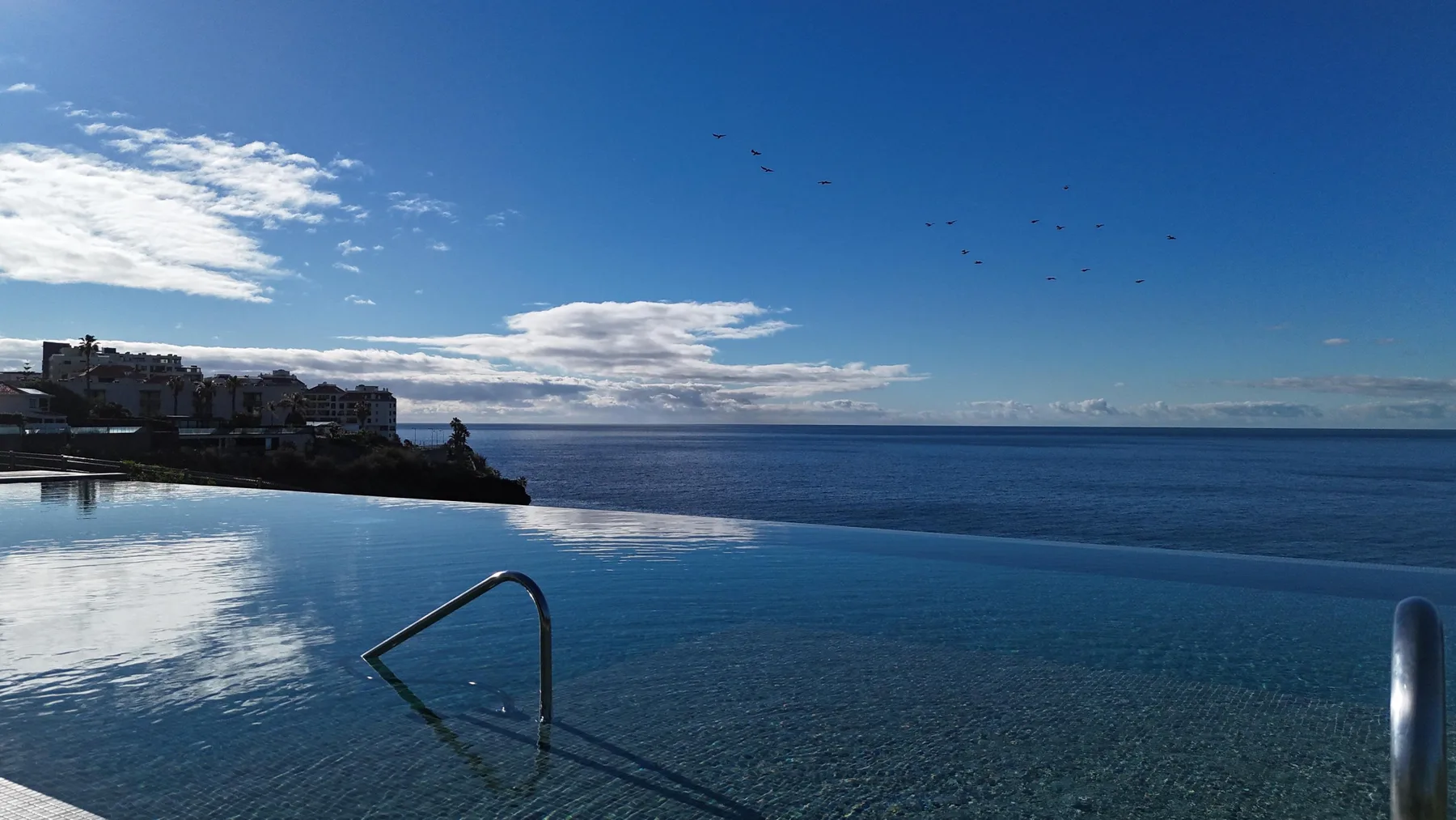 Una piscina infinita da al océano bajo un cielo parcialmente nublado.