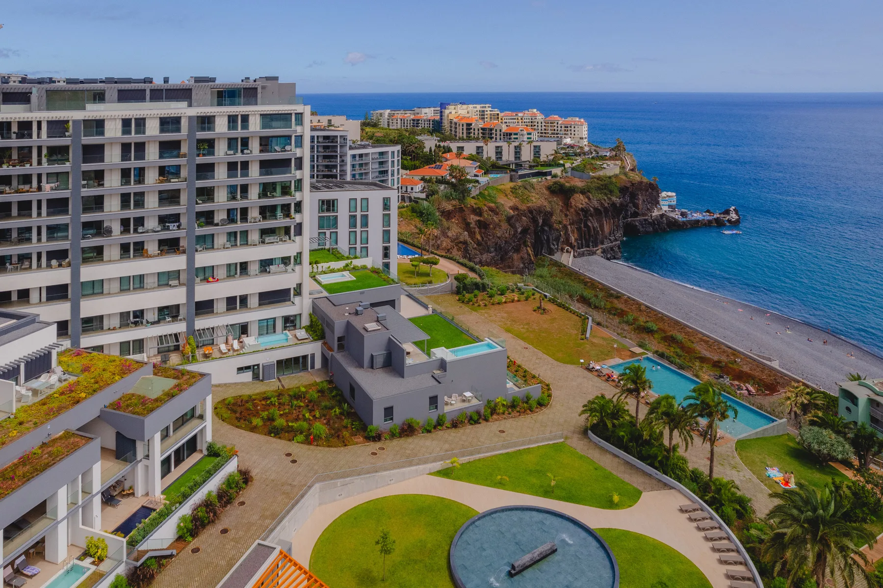 Residencias modernas junto al mar dominan una costa rocosa y una piscina curva.