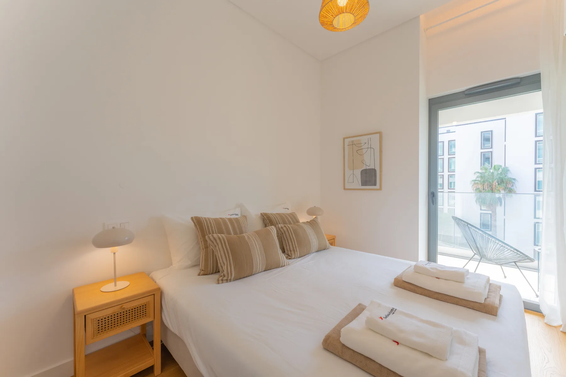Un dormitorio luminoso con una cama, una mesita de noche y una puerta de cristal que da a un balcón.