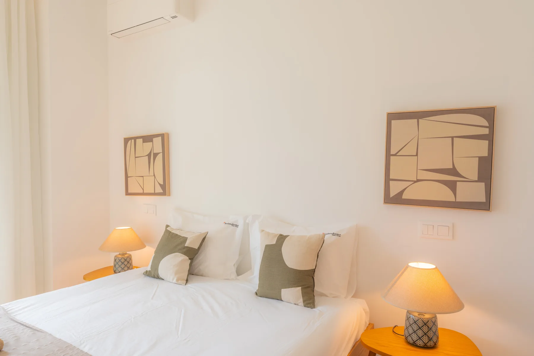 Un dormitorio luminoso tiene una cama blanca, mesitas de noche y arte abstracto en la pared.