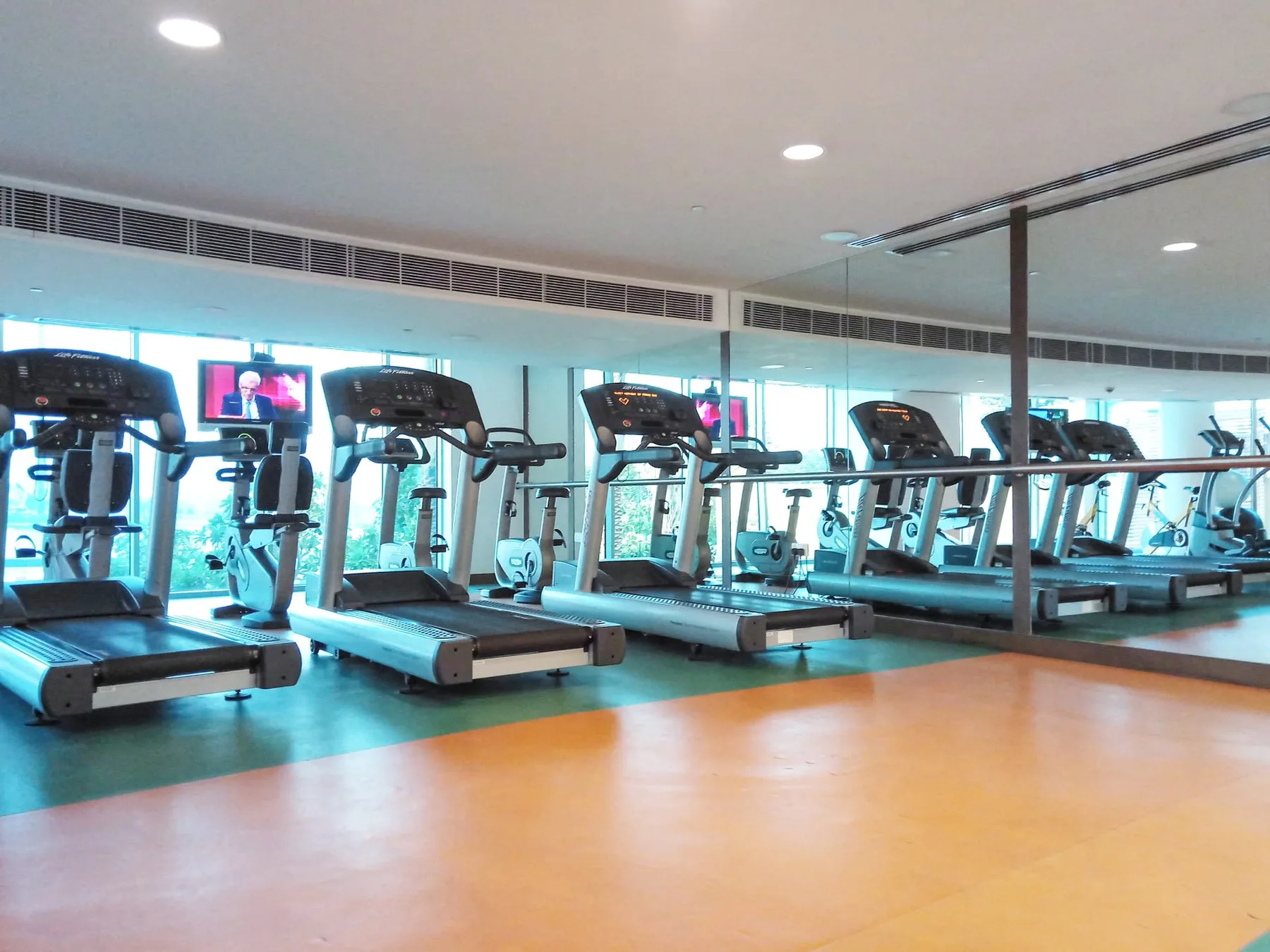 Un gimnasio con caminadoras y otros equipos de ejercicio junto a paredes con espejos.
