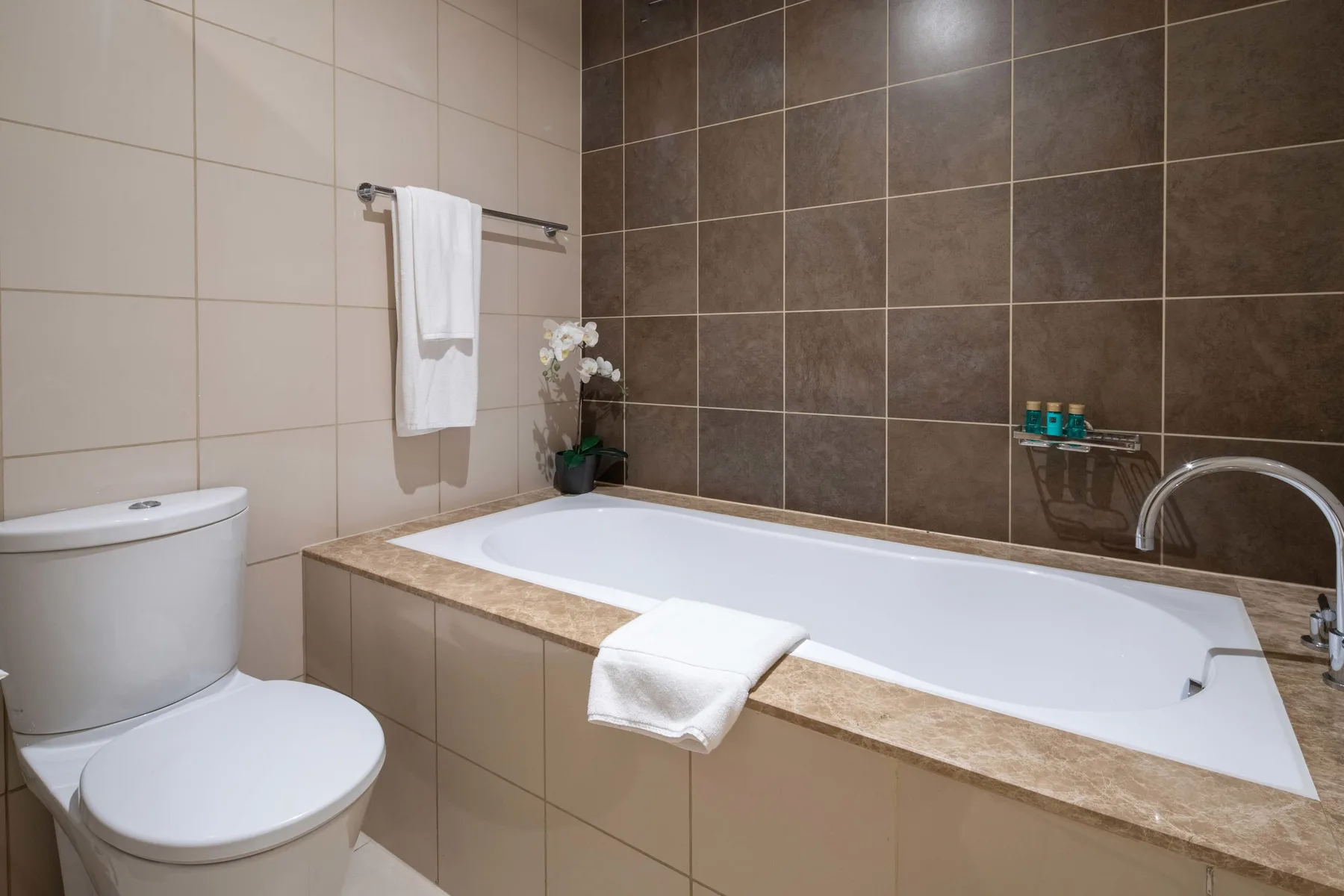 Un baño alicatado con bañera, inodoro y toallas dobladas.