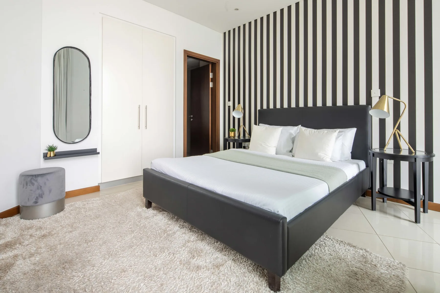 Un dormitorio con una cama grande, una pared decorativa a rayas y una alfombra clara.