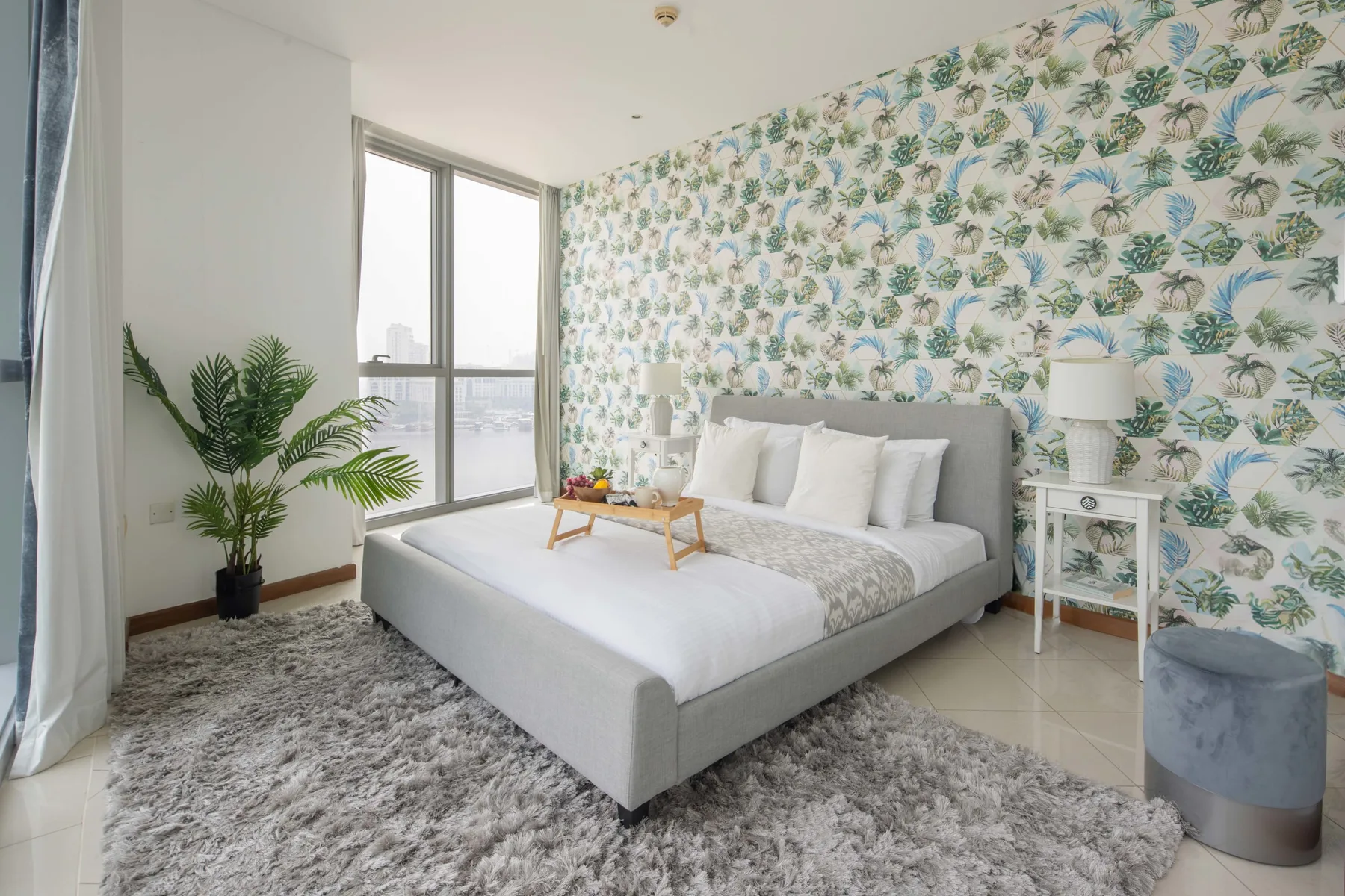 Un dormitorio con una cama, papel tapiz con hojas y una ventana grande.