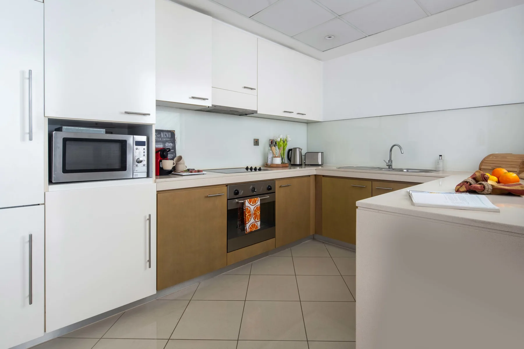 Una cocina moderna con armarios blancos, muebles inferiores en tonos de madera y suelo de baldosas.