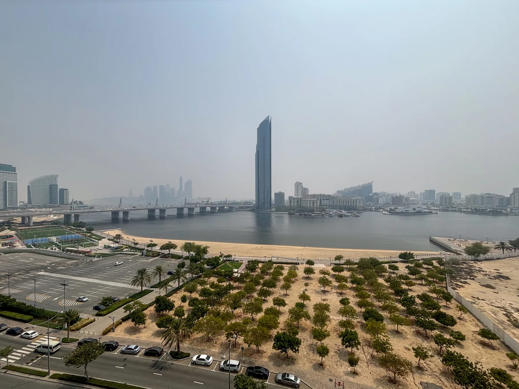 Un horizonte urbano junto al agua y un puente se alzan sobre un río y una orilla ajardinada.