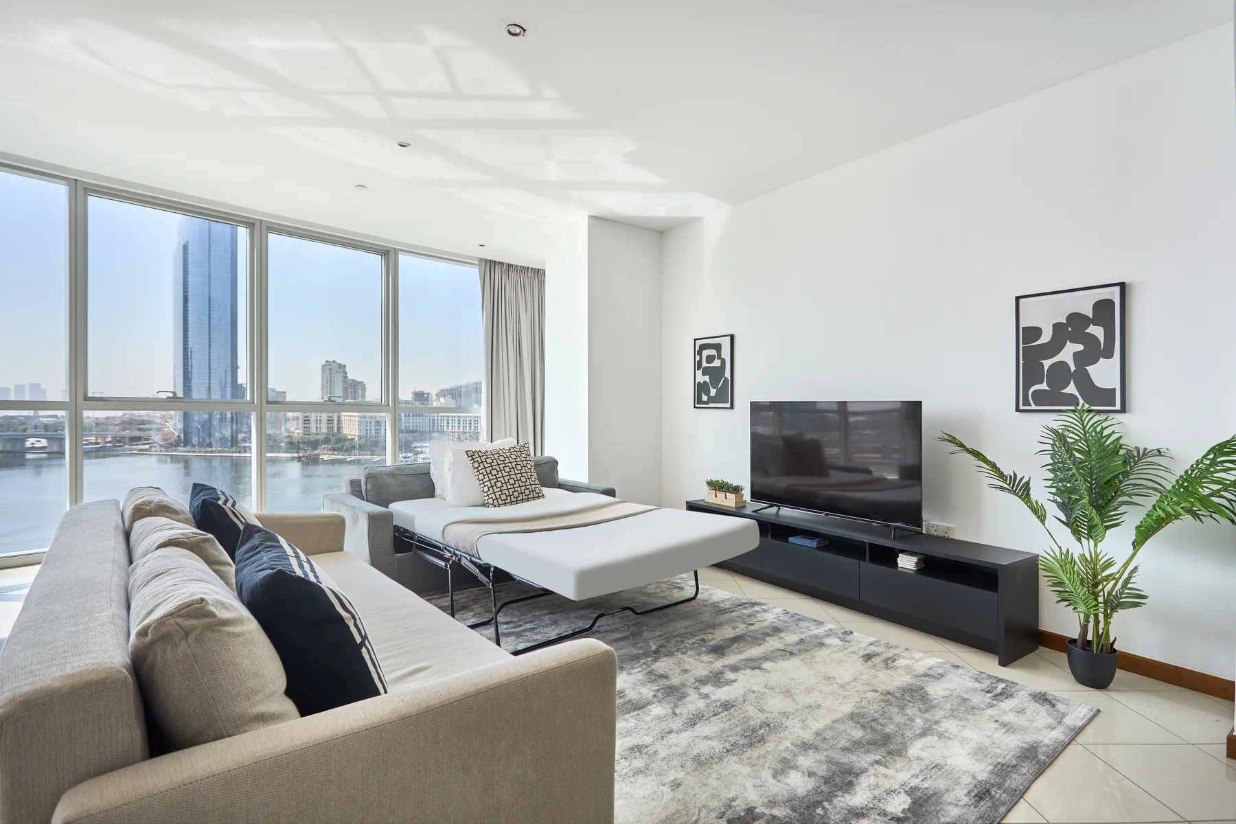 Una sala luminosa con asientos, un televisor y grandes ventanas con vistas al agua.