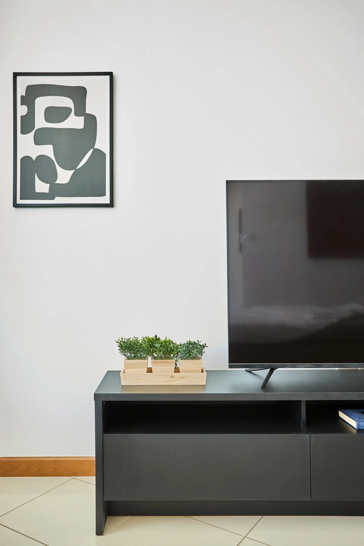 Una pared de sala de estar tiene un televisor sobre un mueble oscuro y una obra enmarcada.