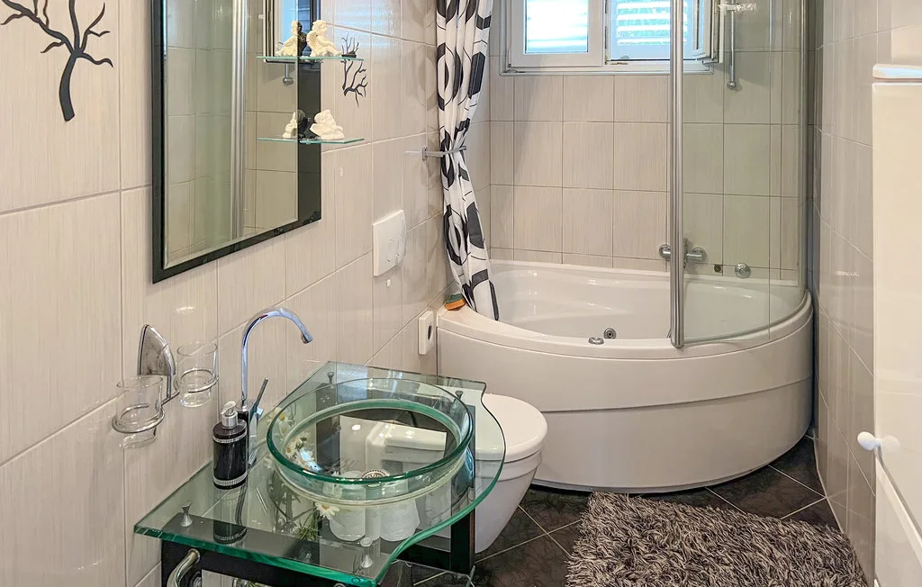 A tiled bathroom with a curved bathtub and glass sink.