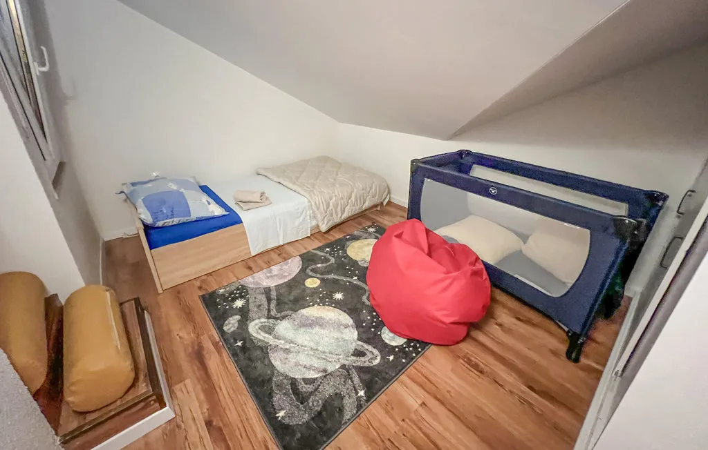 A small bedroom with a single bed, a playpen, and a space-themed rug.