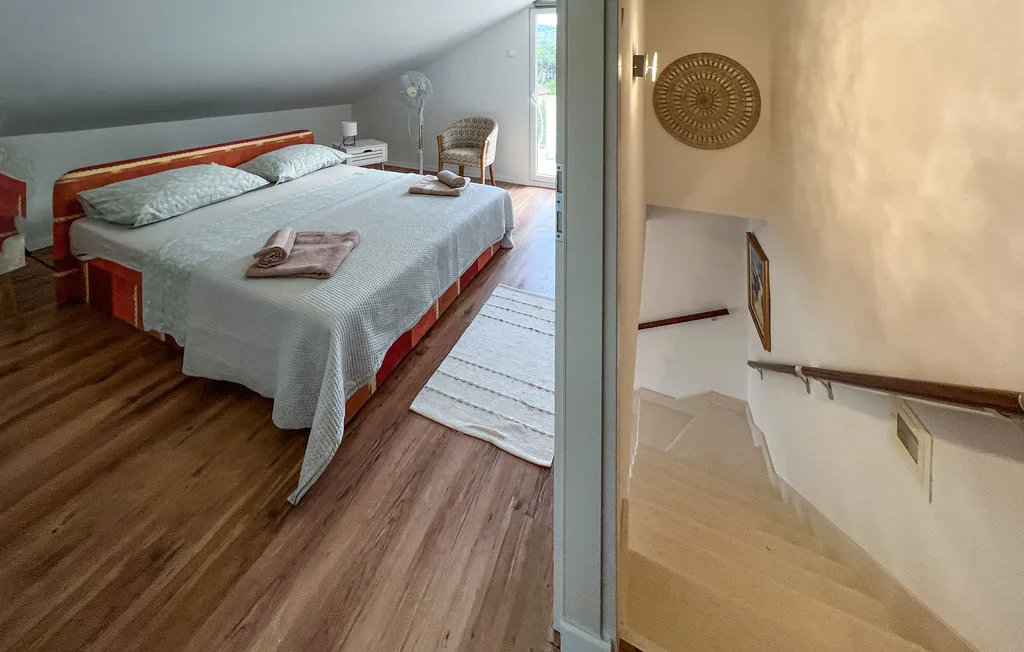 A bedroom with a neatly made bed beside a doorway overlooking a staircase.
