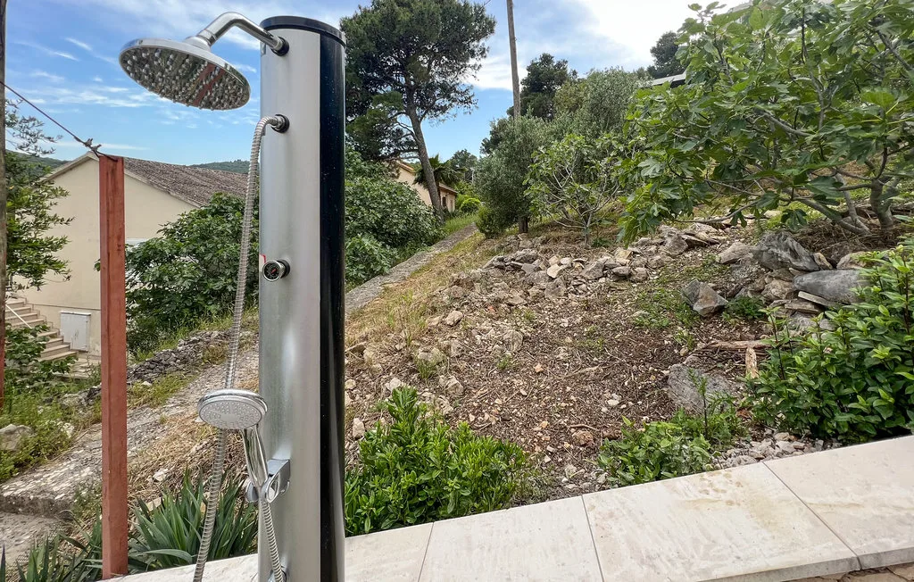 An outdoor shower stands beside a rocky garden on a tiled patio.