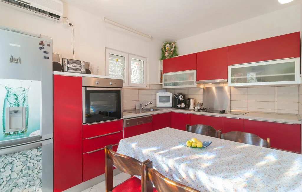 A kitchen with red cabinets, appliances, and a dining table.