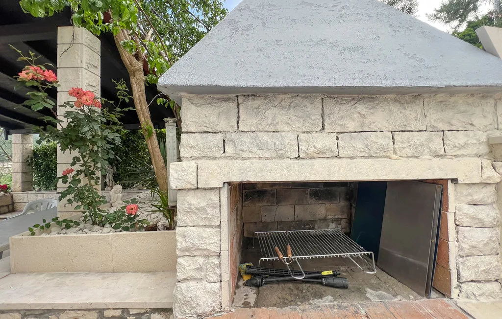 An outdoor stone fireplace stands beside a planted garden area.