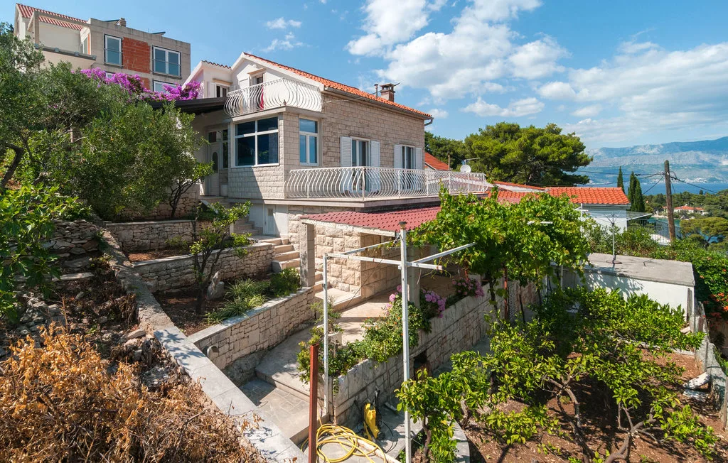 A multi-level house with balconies sits among terraced gardens.