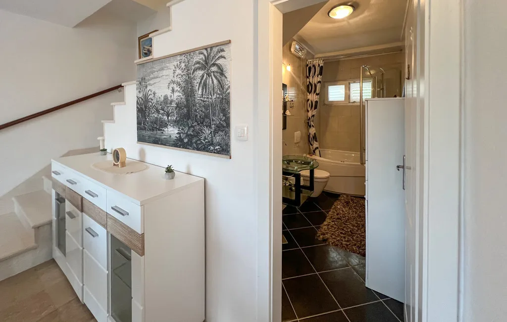 A hallway cabinet stands beside an open bathroom with a bathtub and dark tiled floor.