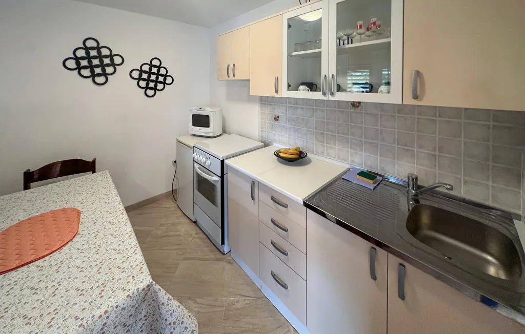 A compact kitchen with white cabinets, a stove, and a stainless-steel sink.