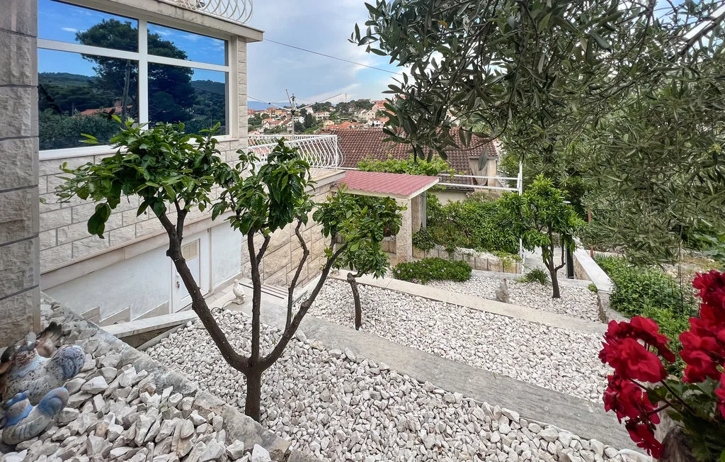 A landscaped garden with a stone path, shrubs, and trees beside a house.