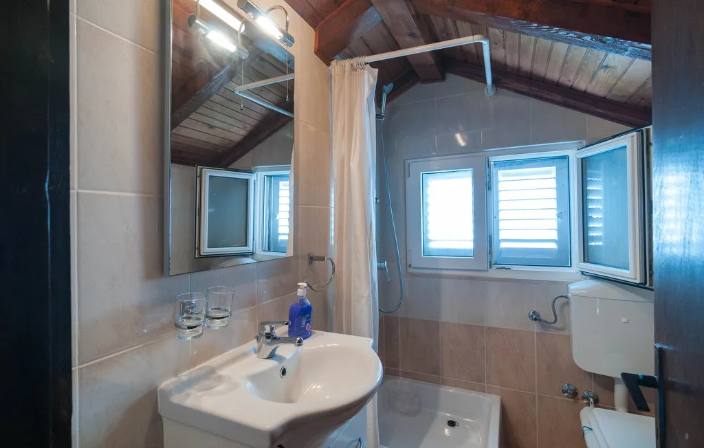 A bathroom with a sink, mirror, and shower beneath a sloped ceiling.