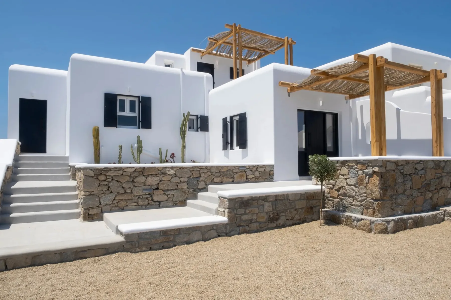 A white building with a stone base, shaded entrance, and outdoor steps.