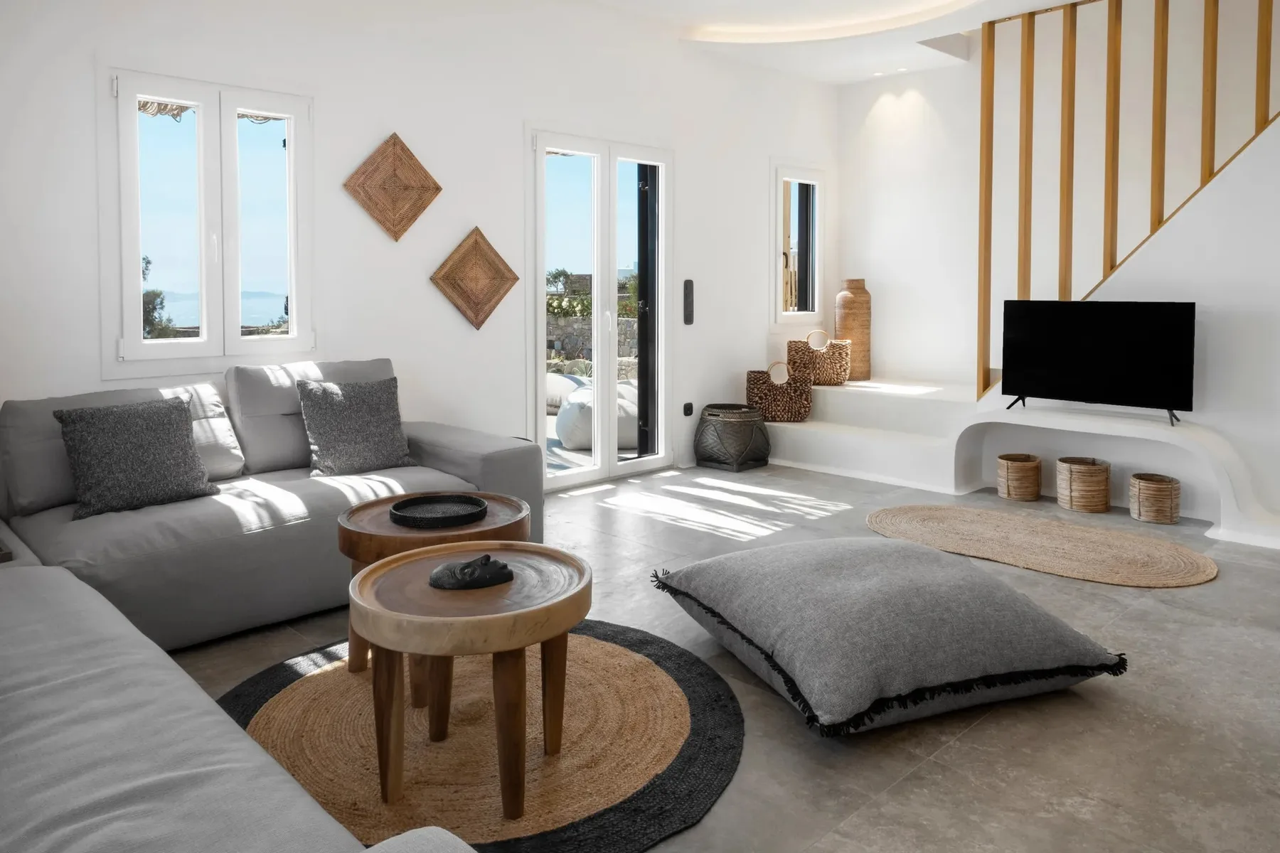 A bright living room with gray seating, round tables, and a television.
