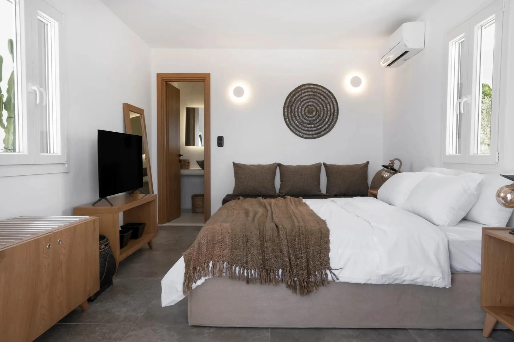 A bright bedroom with a bed, television, and windows.