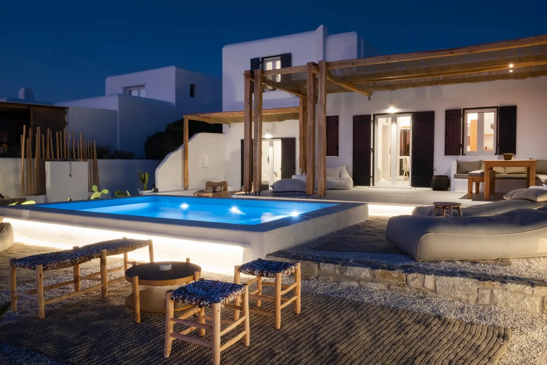 A villa patio with a lit swimming pool, outdoor seating, and a wooden pergola.
