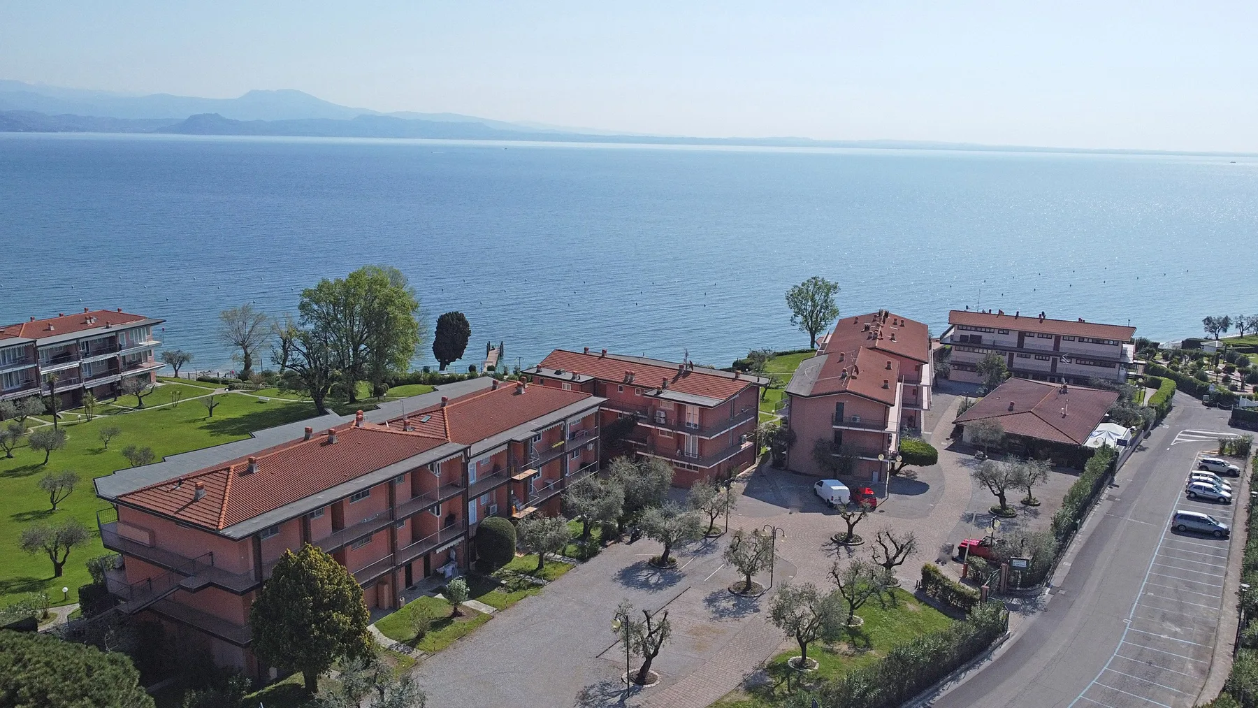Aerial view of low-rise buildings and landscaped grounds beside a broad waterfront.