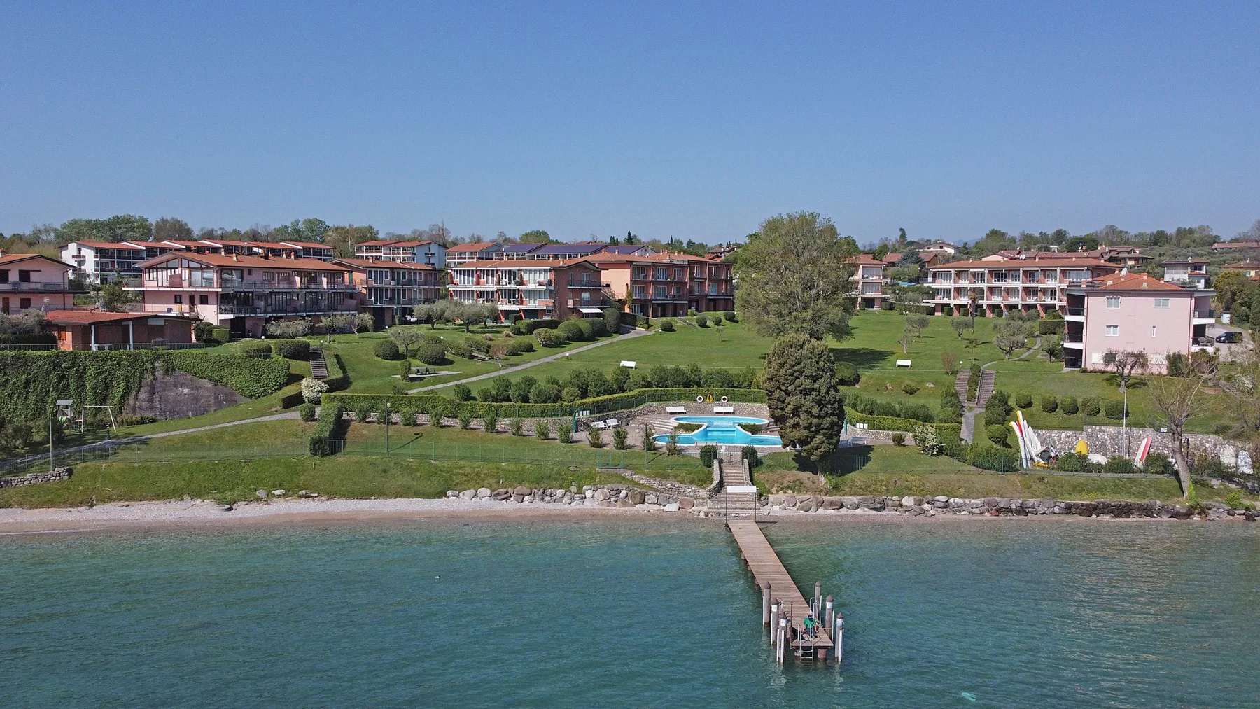 A landscaped lakeside resort with buildings, gardens, and a pier extending into the water.
