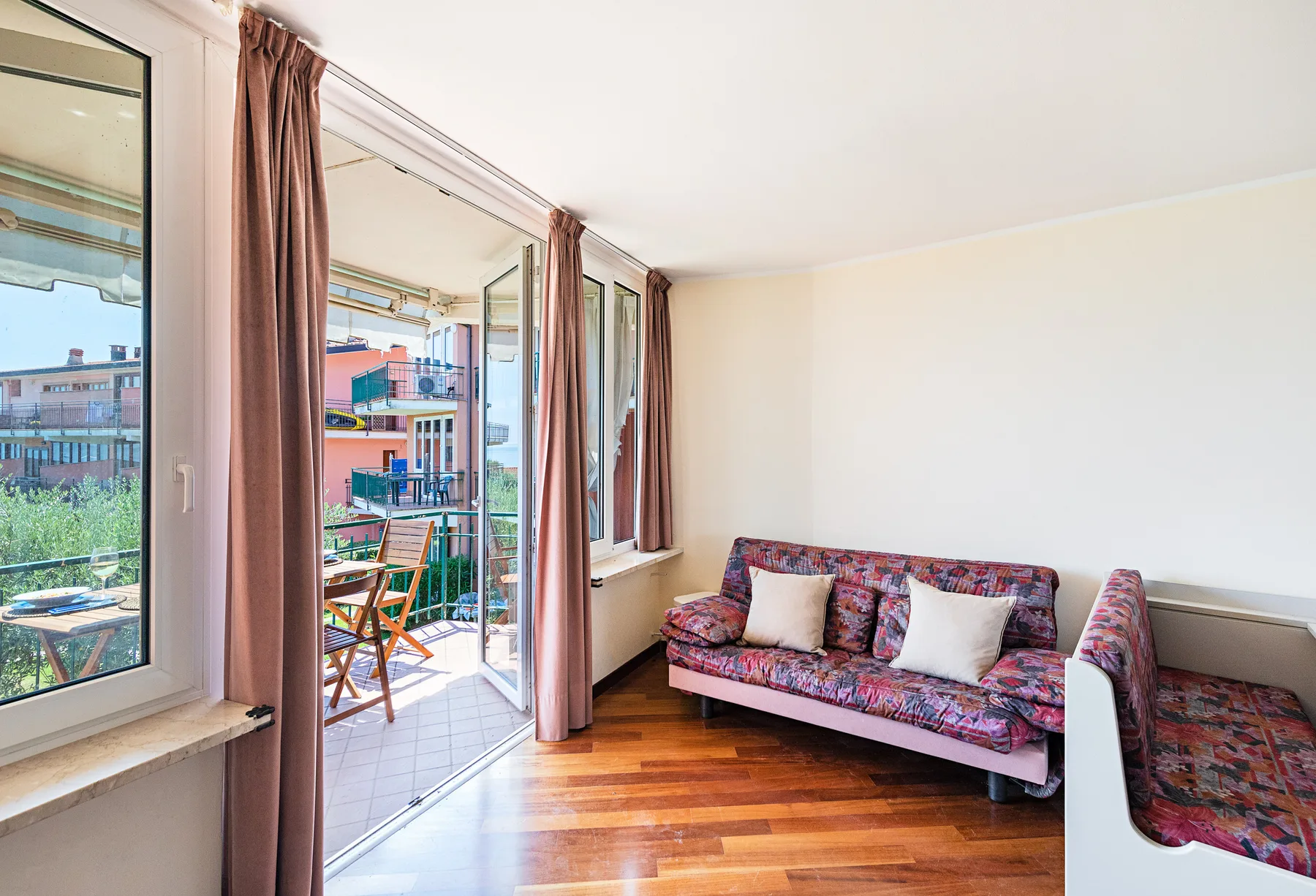 A living room with a patterned sofa beside open glass doors leading to a balcony.