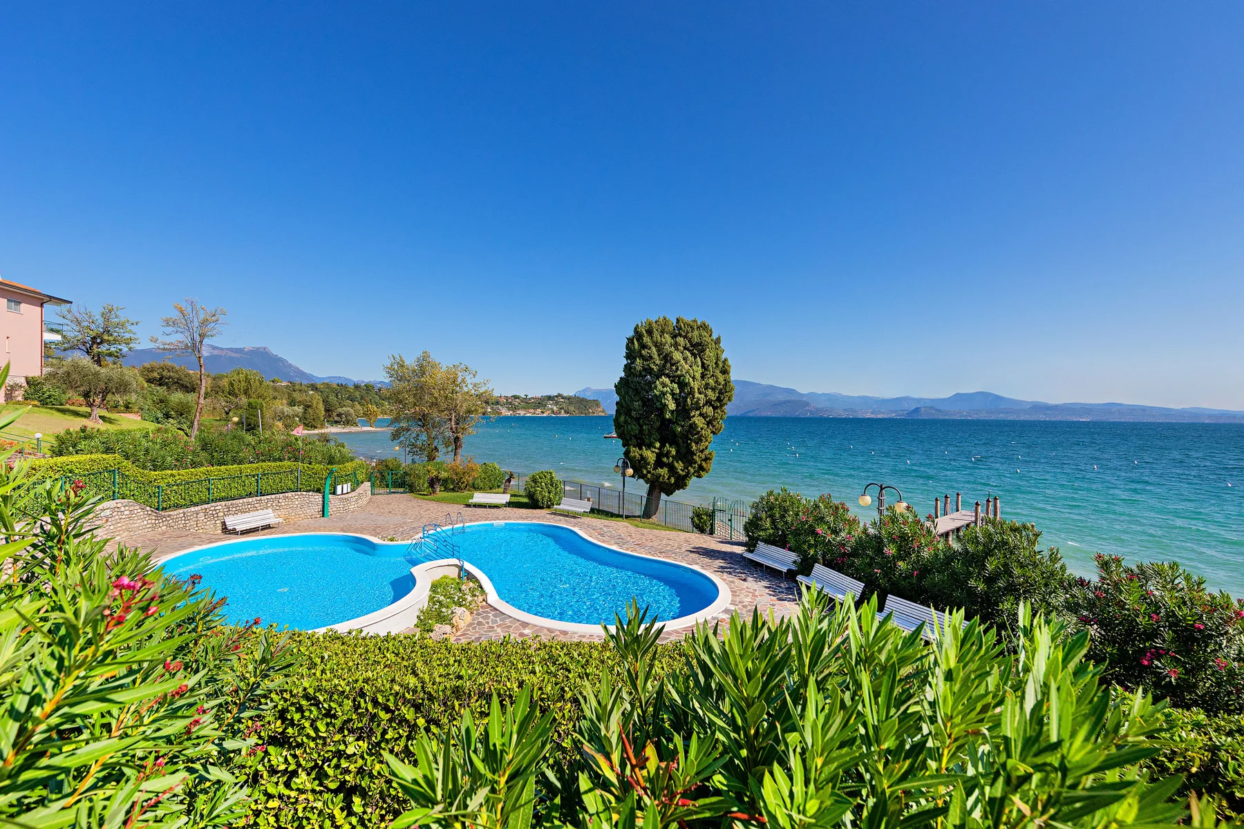 A swimming pool overlooks a lake, surrounded by greenery and mountain views.