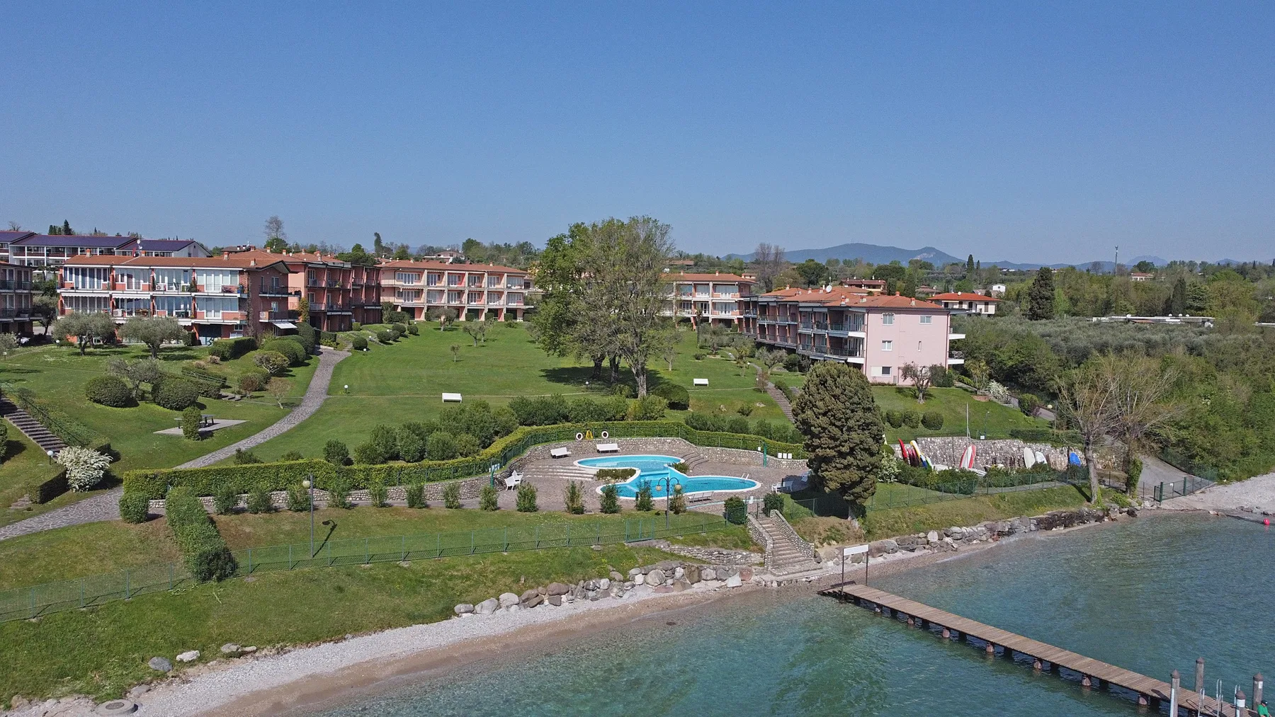 A landscaped resort grounds with a swimming pool beside the waterfront and a pier.