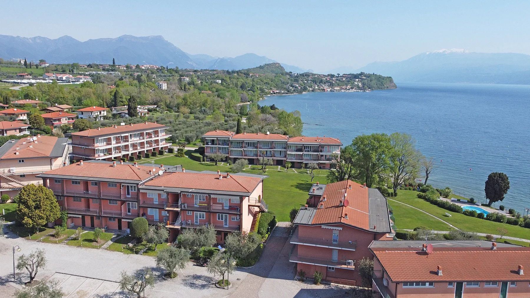 Aerial view of red-roofed buildings beside a lake, with mountains in the distance.