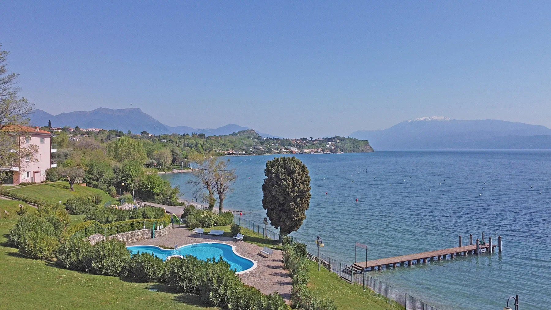 A lakeside landscape with a swimming pool, gardens, and a pier.