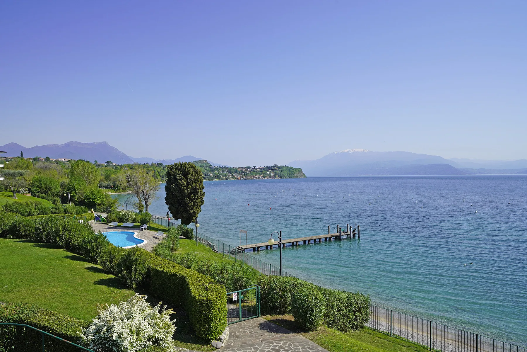 A landscaped lakeside garden overlooks the water, with a small pier extending from shore.