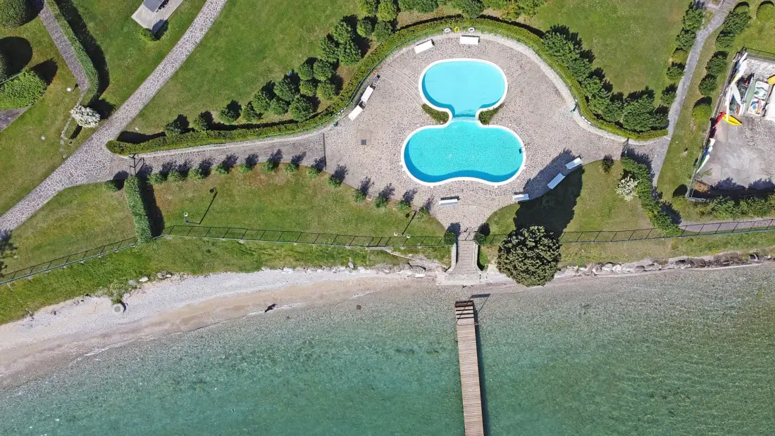 An aerial view shows a two-lobed swimming pool beside a beach and a narrow pier.