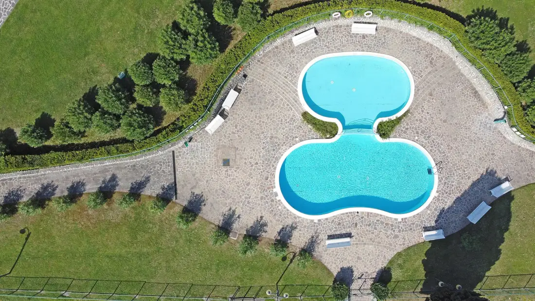 An aerial view shows two connected swimming pools surrounded by a paved pool deck.