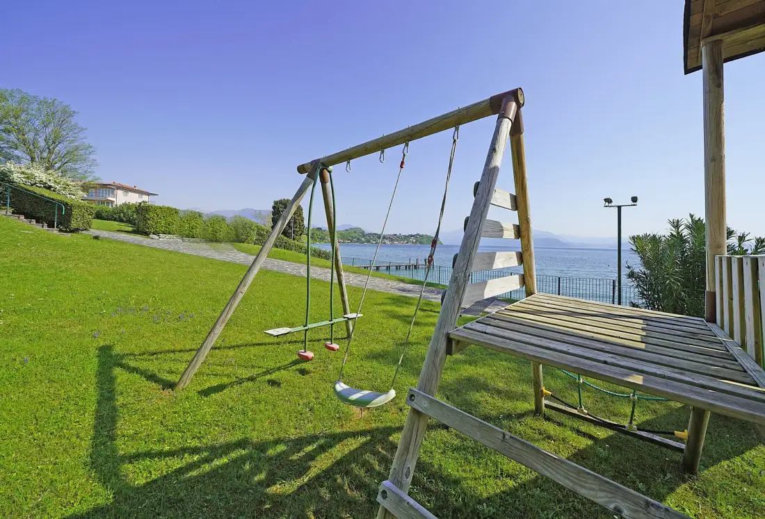 A grassy waterfront area features a wooden swing set beside a raised seating platform.